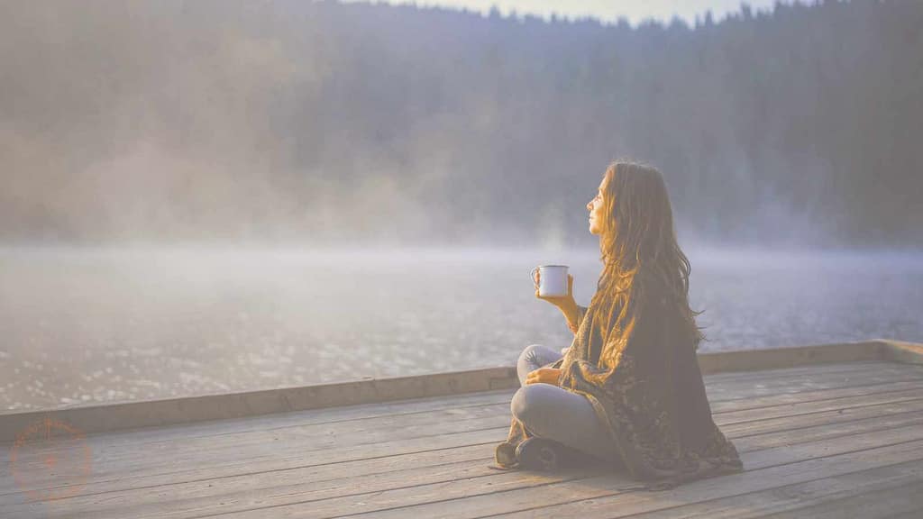 spiritualität ist heimkommen frau sitzt mit tasse auf steeg am wasser