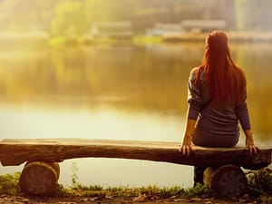 eine frau sitzt nachdenklich auf einer bank am wasser schamanismus online kurs